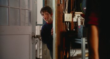 Movie still from “Diary of a Wimpy Kid” (2010), directed by Thor Freudenthal – A young boy peeks out from behind a door; Medium shot, Over the shoulder angle