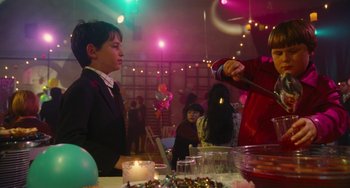 Movie still from “Diary of a Wimpy Kid” (2010), directed by Thor Freudenthal – A woman standing in front of a table with food on it; Medium shot, Over the shoulder angle