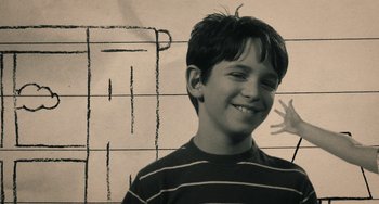 Movie still from “Diary of a Wimpy Kid” (2010), directed by Thor Freudenthal – A young boy smiling in front of a wall; Medium shot, High angle