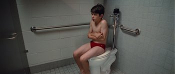 Movie still from “Diary of a Wimpy Kid: Rodrick Rules” (2011), directed by David Bowers – A young boy sitting on top of a white toilet seat; Medium shot, High angle