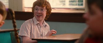 Movie still from “Diary of a Wimpy Kid: Rodrick Rules” (2011), directed by David Bowers – A young man sitting at a table with a smile on his face; Medium shot, Over the shoulder angle