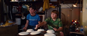 Movie still from “Diary of a Wimpy Kid: Rodrick Rules” (2011), directed by David Bowers – Two young boys sitting at a table with plates of cake; Medium shot, High angle