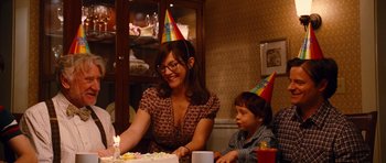 Movie still from “Diary of a Wimpy Kid: Rodrick Rules” (2011), directed by David Bowers – A woman sitting at a table in front of a birthday cake; Medium shot, Over the shoulder angle