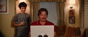 Movie still from “Diary of a Wimpy Kid: Rodrick Rules” (2011), directed by David Bowers – A man in a red shirt is sitting in front of an open laptop computer; Medium shot, Low angle