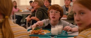 Movie still from “Diary of a Wimpy Kid: Rodrick Rules” (2011), directed by David Bowers – A boy eating a sandwich at a table with other people watching; Close Up shot, Over the shoulder angle