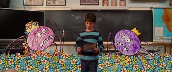 Movie still from “Diary of a Wimpy Kid: Rodrick Rules” (2011), directed by David Bowers – A young boy reading a paper in front of a chalkboard; Wide shot, Over the shoulder angle