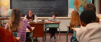 Movie still from “Diary of a Wimpy Kid: Rodrick Rules” (2011), directed by David Bowers – A boy sitting at a desk in front of a chalkboard; Wide shot, High angle