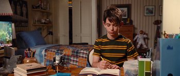 Movie still from “Diary of a Wimpy Kid: Rodrick Rules” (2011), directed by David Bowers – A young boy sitting at a table writing in a book; Medium shot, High angle