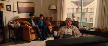Movie still from “Diary of a Wimpy Kid: Rodrick Rules” (2011), directed by David Bowers – A man sitting in a chair with two other people watching; Wide shot, Over the shoulder angle