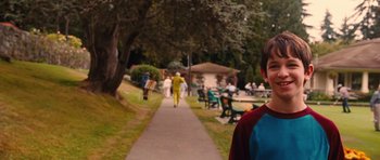 Movie still from “Diary of a Wimpy Kid: Rodrick Rules” (2011), directed by David Bowers – A man standing on a sidewalk near a park; Medium shot, Over the shoulder angle