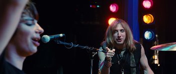 Movie still from “Diary of a Wimpy Kid: Rodrick Rules” (2011), directed by David Bowers – A woman holding a microphone on a stage; Medium shot, Over the shoulder angle