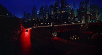Movie still from “Dick Tracy” (1990), directed by Warren Beatty – A car driving down a street at night with a city skyline in the background; Extreme Wide shot, High angle