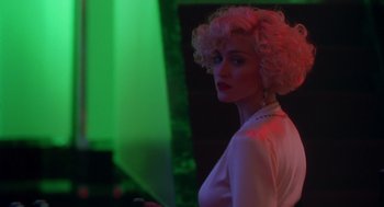 Movie still from “Dick Tracy” (1990), directed by Warren Beatty – A woman with blonde curly hair standing in front of a green light; Close Up shot, Over the shoulder angle
