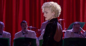 Movie still from “Dick Tracy” (1990), directed by Warren Beatty – A woman in a black dress standing in front of a microphone; Medium shot, Over the shoulder angle