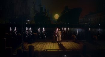 Movie still from “Dick Tracy” (1990), directed by Warren Beatty – A man standing on a dock next to a body of water at night; Extreme Wide shot, High angle