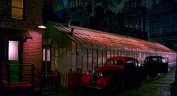 Movie still from “Dick Tracy” (1990), directed by Warren Beatty – An old red car parked in front of a building at night; Extreme Wide shot, Low angle