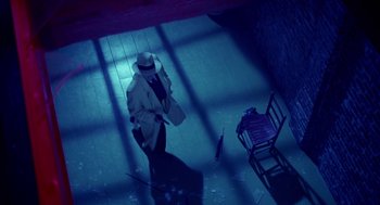 Movie still from “Dick Tracy” (1990), directed by Warren Beatty – A man wearing a hat and a coat standing next to a chair and umbrella; Wide shot, High angle