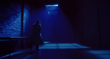 Movie still from “Dick Tracy” (1990), directed by Warren Beatty – A man in a trench coat and a top hat walking in a dark room; Wide shot, High angle