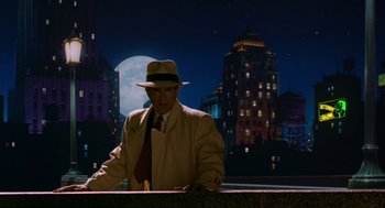 Movie still from “Dick Tracy” (1990), directed by Warren Beatty – A man wearing a hat and a suit standing in front of buildings; Wide shot, Over the shoulder angle