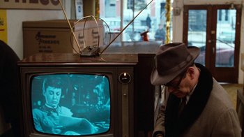 Movie still from “Diner” (1982), directed by Barry Levinson – A man in a hat is looking at a television; Medium shot, Over the shoulder angle