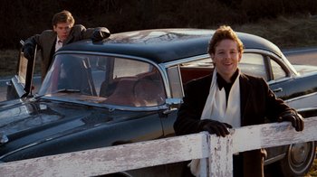 Movie still from “Diner” (1982), directed by Barry Levinson – A man leaning on a fence next to an old car; Medium shot, Low angle