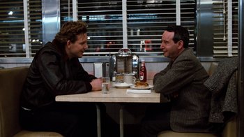 Movie still from “Diner” (1982), directed by Barry Levinson – Two men sitting at a table in front of a drink; Medium shot, Over the shoulder angle