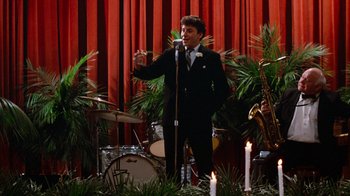 Movie still from “Diner” (1982), directed by Barry Levinson – A man in a suit and tie singing into a microphone; Wide shot, High angle