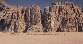 Movie still from “Dinosaur” (2000), directed by Eric Leighton – A group of animals walking on top of a sandy beach; Extreme Wide shot, High angle