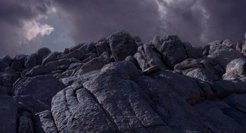 Movie still from “Dinosaur” (2000), directed by Eric Leighton – A large rock formation with a cloudy sky in the background; Extreme Wide shot, Low angle