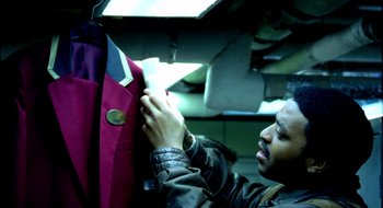 Movie still from “Dirty Pretty Things” (2002), directed by Stephen Frears – A man is looking at a jacket on a hanger; Medium shot, Over the shoulder angle
