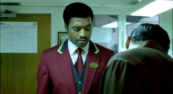 Movie still from “Dirty Pretty Things” (2002), directed by Stephen Frears – A man wearing a red suit and a red tie; Medium shot, Over the shoulder angle