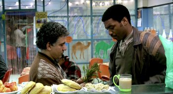 Movie still from “Dirty Pretty Things” (2002), directed by Stephen Frears – Two men sitting at a table with a plate of food; Medium shot, Over the shoulder angle