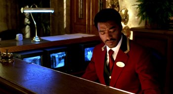 Movie still from “Dirty Pretty Things” (2002), directed by Stephen Frears – A man in a red suit playing a piano; Medium shot, High angle