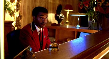 Movie still from “Dirty Pretty Things” (2002), directed by Stephen Frears – A man sitting at a table in front of a bell; Medium shot, Low angle