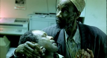 Movie still from “Dirty Pretty Things” (2002), directed by Stephen Frears – An older man with a beard is grooming a younger man's face; Close Up shot, High angle