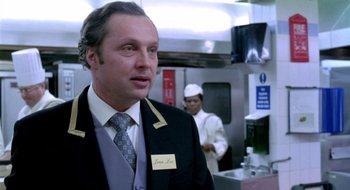 Movie still from “Dirty Pretty Things” (2002), directed by Stephen Frears – A man in a suit and tie standing in a kitchen; Medium shot, Over the shoulder angle