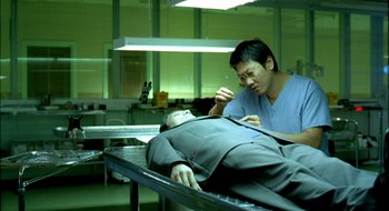 Movie still from “Dirty Pretty Things” (2002), directed by Stephen Frears – A man in a room with a man lying on a table; Medium shot, High angle