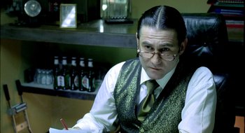 Movie still from “Dirty Pretty Things” (2002), directed by Stephen Frears – A man in a vest and tie sitting at a table; Close Up shot, Over the shoulder angle
