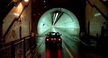 Movie still from “Dirty Pretty Things” (2002), directed by Stephen Frears – A car is driving through a tunnel in the dark; Extreme Wide shot, High angle