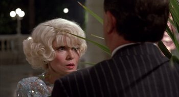 Movie still from “Dirty Rotten Scoundrels” (1988), directed by Frank Oz – An older woman with blonde hair looking at a younger man in pinstriped suit; Close Up shot, Over the shoulder angle