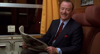 Movie still from “Dirty Rotten Scoundrels” (1988), directed by Frank Oz – A man in a suit and tie reading a newspaper; Medium shot, Low angle