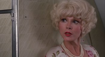 Movie still from “Dirty Rotten Scoundrels” (1988), directed by Frank Oz – An older woman with blonde hair wearing a dress and pearls; Close Up shot, Low angle