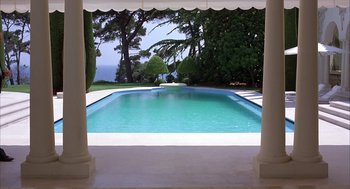 Movie still from “Dirty Rotten Scoundrels” (1988), directed by Frank Oz – An empty swimming pool surrounded by pillars and trees; Extreme Wide shot, High angle