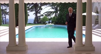 Movie still from “Dirty Rotten Scoundrels” (1988), directed by Frank Oz – A man in a suit and tie standing in front of a swimming pool; Wide shot, Low angle