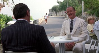 Movie still from “Dirty Rotten Scoundrels” (1988), directed by Frank Oz – Two men sitting at an outdoor table on a sidewalk; Medium shot, Over the shoulder angle