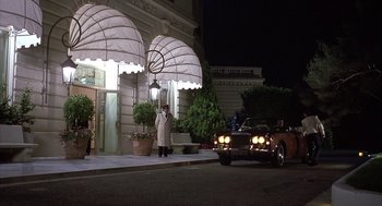 Movie still from “Dirty Rotten Scoundrels” (1988), directed by Frank Oz – A man standing next to a car in front of a building; Wide shot, Low angle