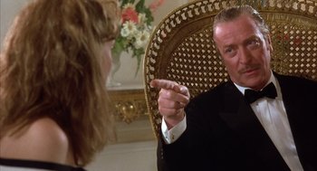Movie still from “Dirty Rotten Scoundrels” (1988), directed by Frank Oz – A man in a black suit is pointing at a woman in a black suit; Close Up shot, Over the shoulder angle