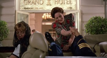 Movie still from “Dirty Rotten Scoundrels” (1988), directed by Frank Oz – A woman in a black and red dress shaking hands with a man in a uniform; Medium shot, Low angle