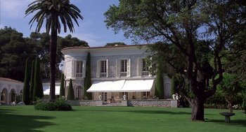 Movie still from “Dirty Rotten Scoundrels” (1988), directed by Frank Oz – A large white building sitting on top of a lush green field; Extreme Wide shot, Low angle