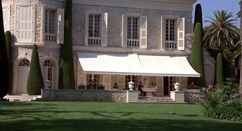 Movie still from “Dirty Rotten Scoundrels” (1988), directed by Frank Oz – Two people are sitting at a table outside of a building; Extreme Wide shot, Low angle